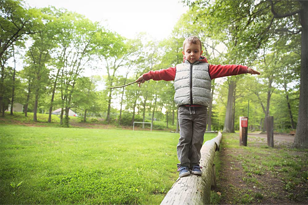 Een jongetje balanceert op een balk in een park