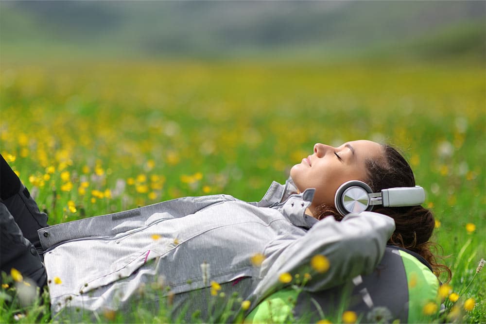 Een vrouw ligt in het gras naar een podcast te luisteren