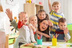 Vijf kinderen knuffelen hun juf en zwaaien naar de camera