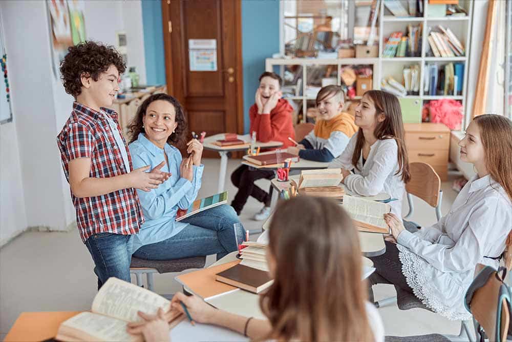 Ee klein groepje kinderen zit in een halve cirkel om de leerkracht heen.