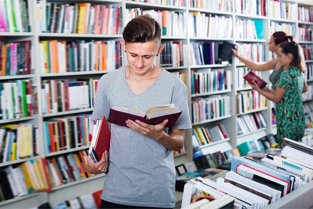 Een lachende tiener leest een boek in de bibliotheek