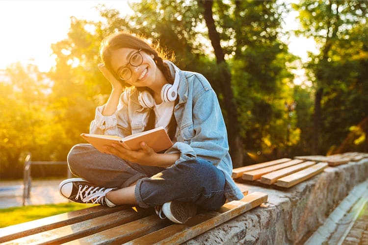 Een tiener leest met een glimlach buiten een boek